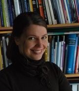 Smiling woman in black shirt in front of a book shelf.