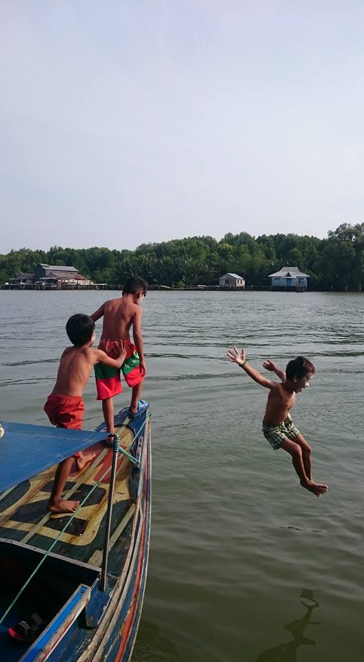 Nuoria poikia hyppäämässä veteen värikkään veneen kannelta.