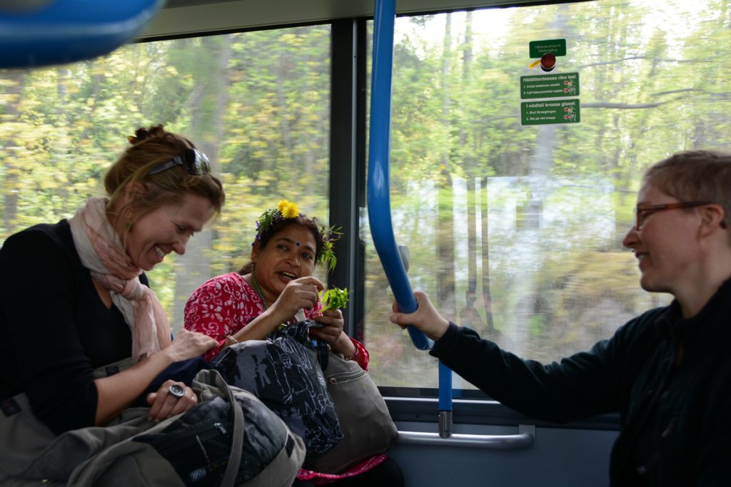 Kolme iloista naista reppuineen istuu linja-autossa.