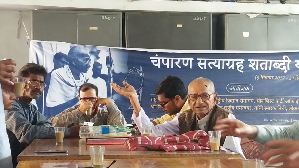 Men with eyeglasses discussing around a table in front of a large poster.