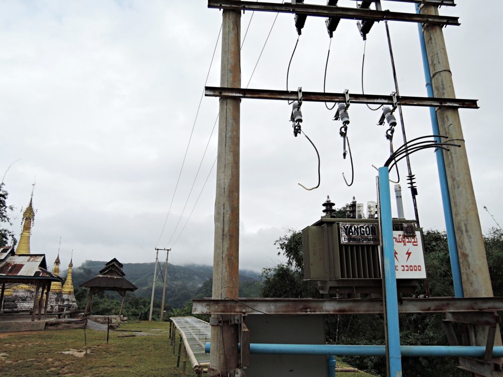 Electricity poles and equipment, some buildings on background.