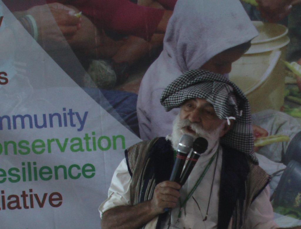 Man with white beard and scarf holding two microphones.