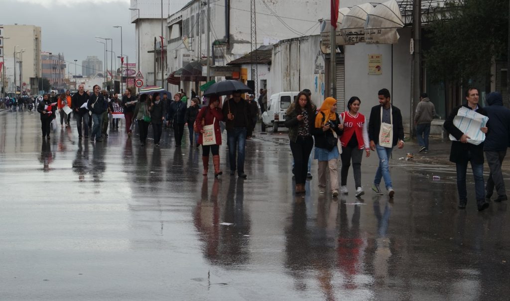 Ihmisiä marssii kadulla sateessa.