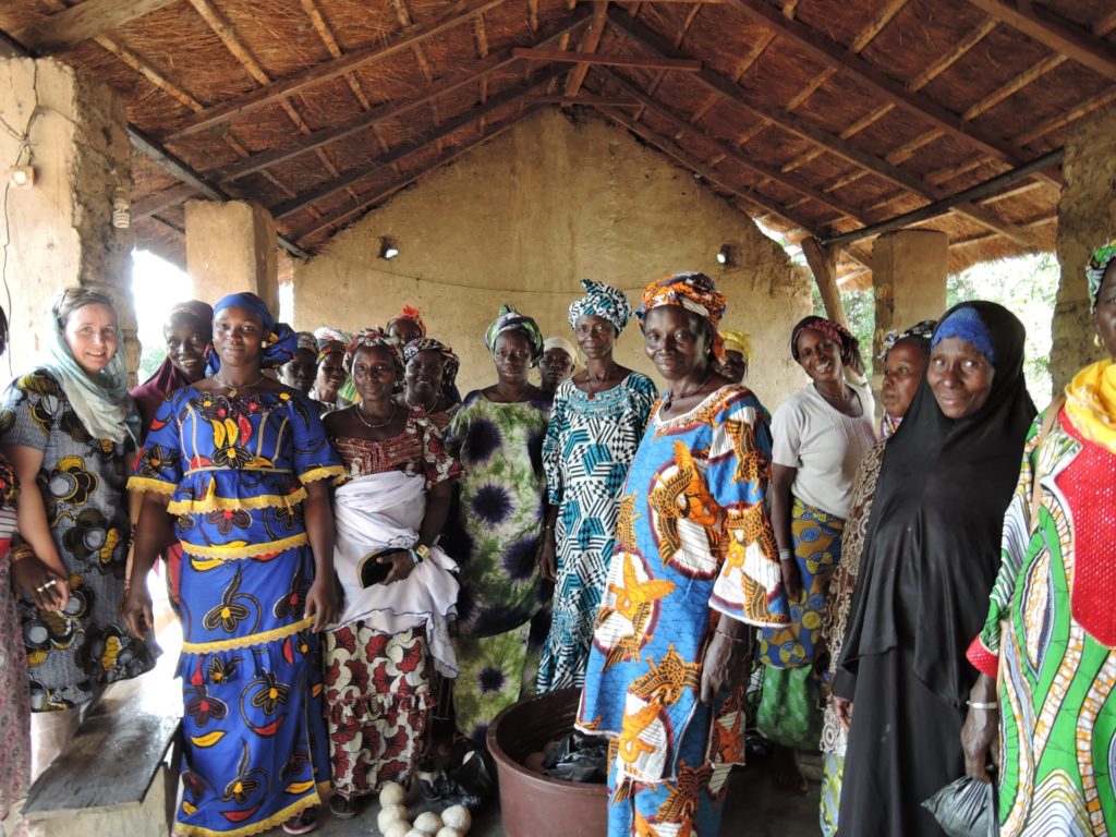 Smiling women in colourful dresses inside a building with grass roof.