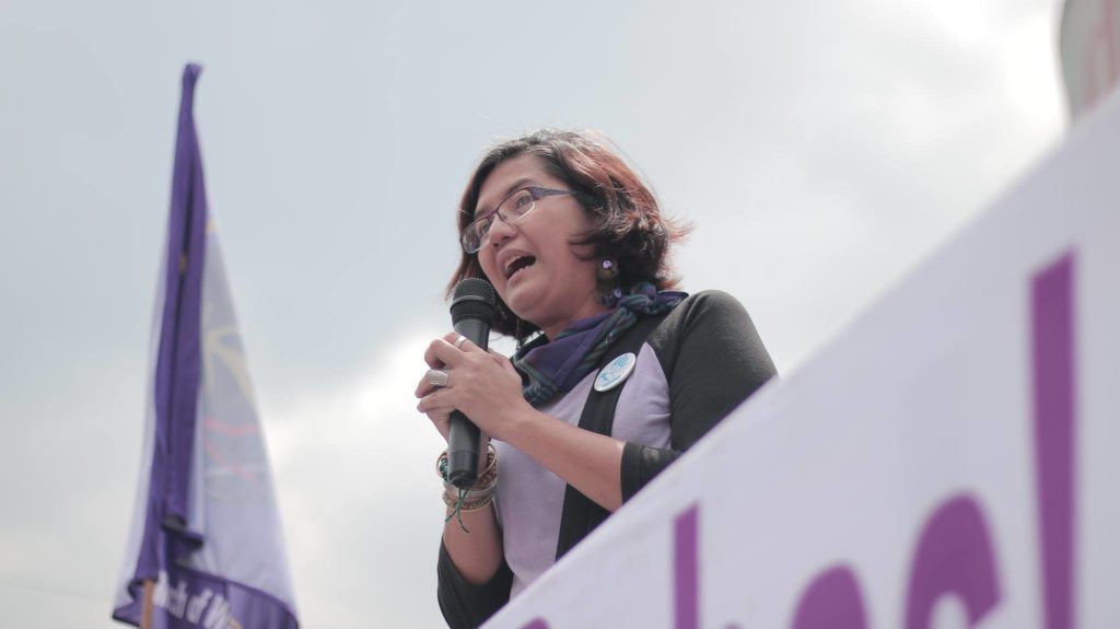 Woman speaking with microphone on a stage.